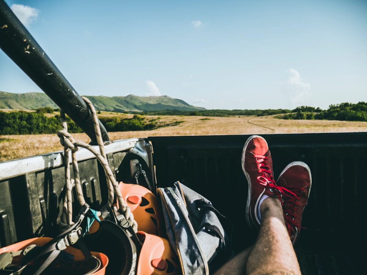Relaxing in a pickup truck with a view of the countryside, featuring red sneakers and climbing gear.