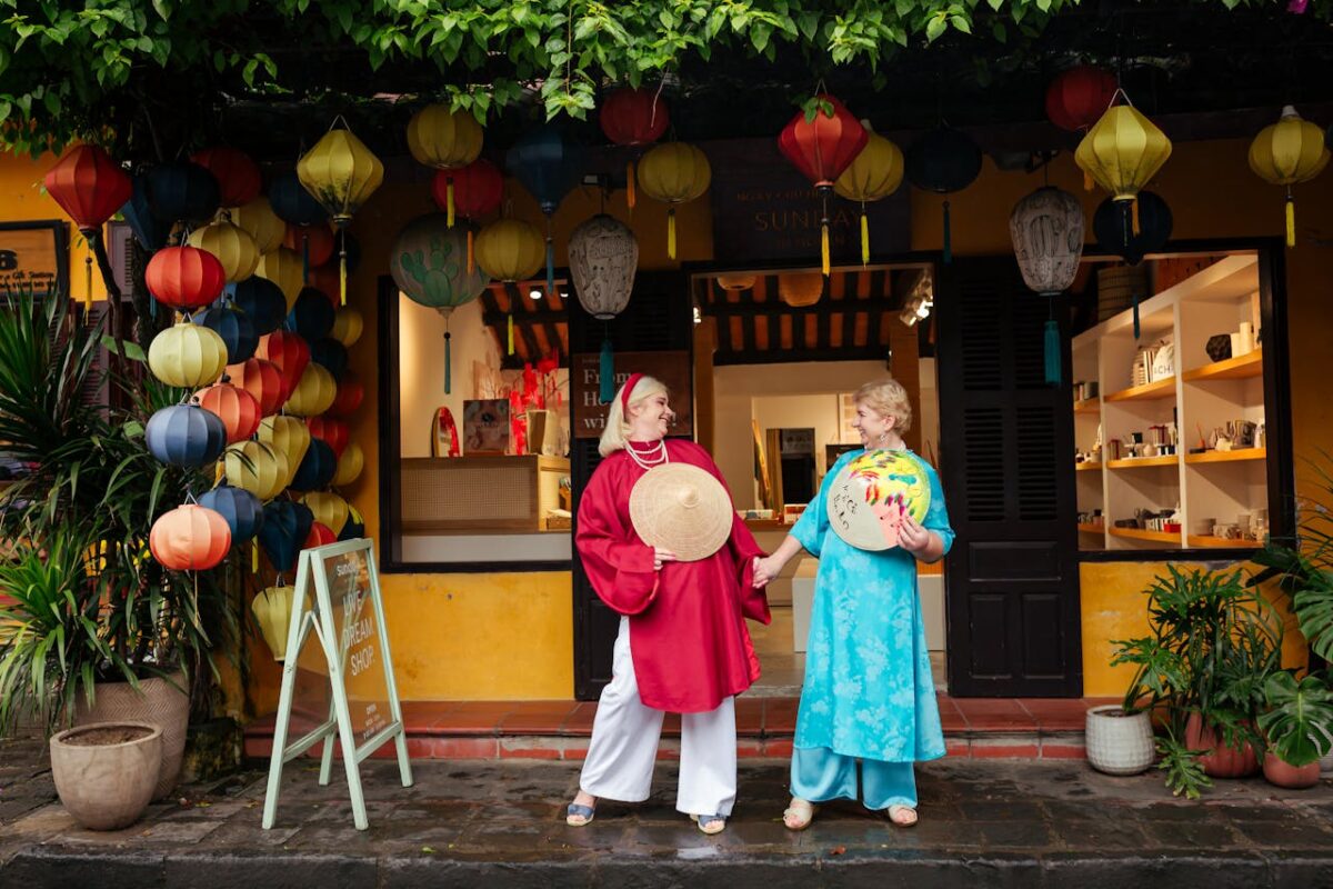 Two people in traditional attire at colorful lantern shop in Hoi An, Vietnam.