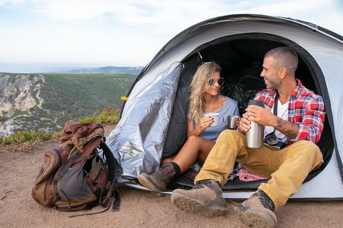 A couple relaxing with coffee in front of their tent overlooking a picturesque landscape in Portugal.